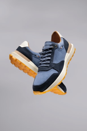 A pair of men’s blue sneakers floating in the air with a gray background.  