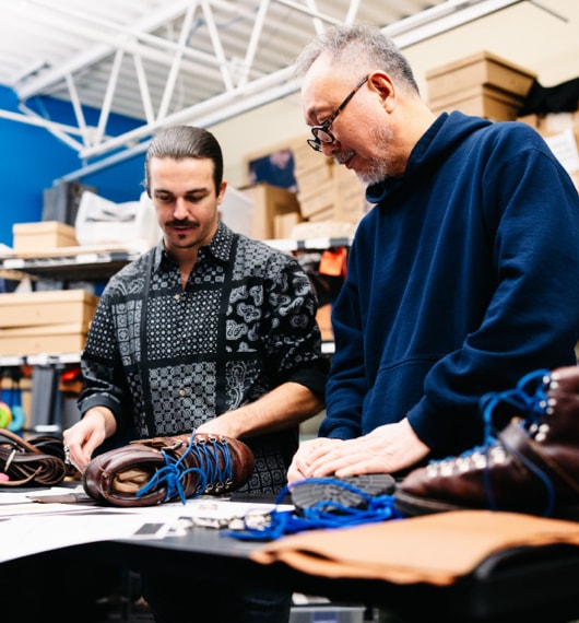 Daiki Suzuki and a colleague standing at a workstation looking at the components of a hiking shoe.