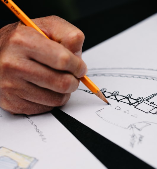 A hand holding a pencil, sketching the design of a hiking shoe on white paper.