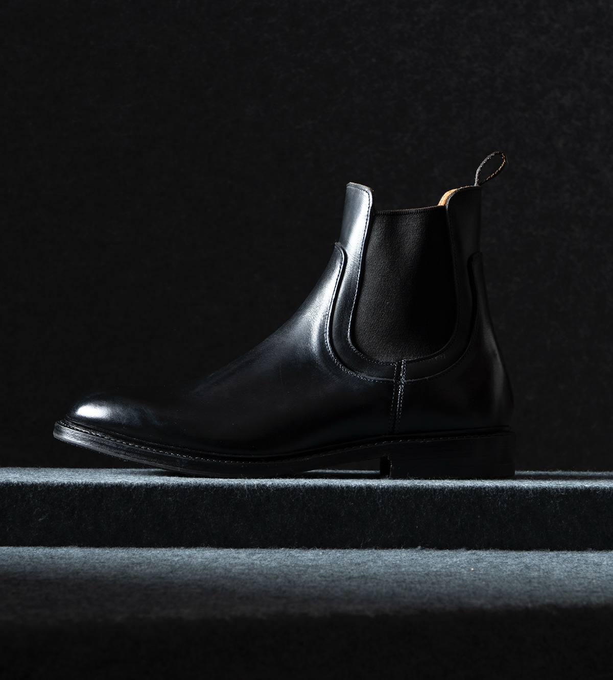 A side view of one men’s black leather Chelsea boot, facing the left