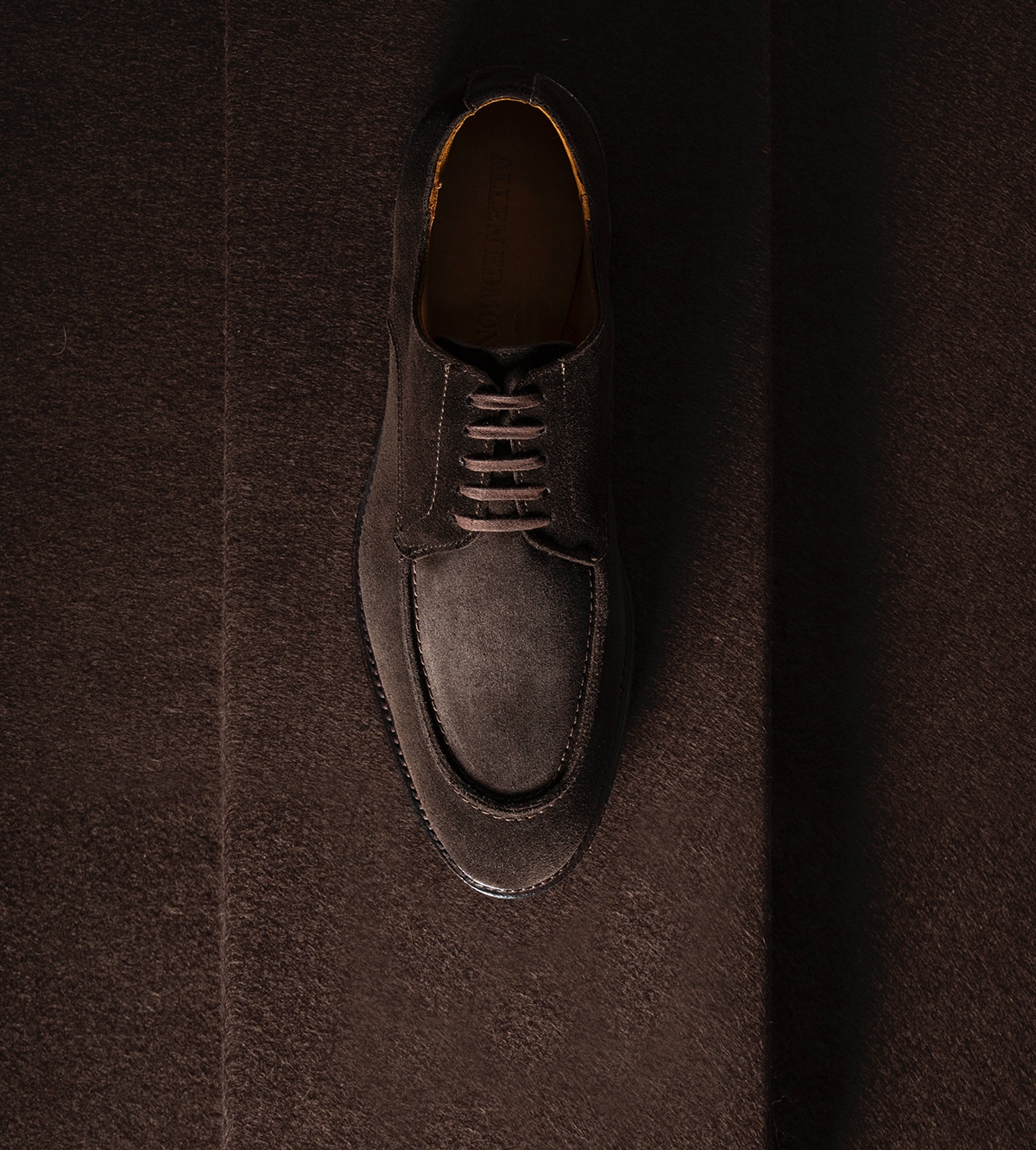 A top view of one men's derby dress shoe in dark brown suede.  