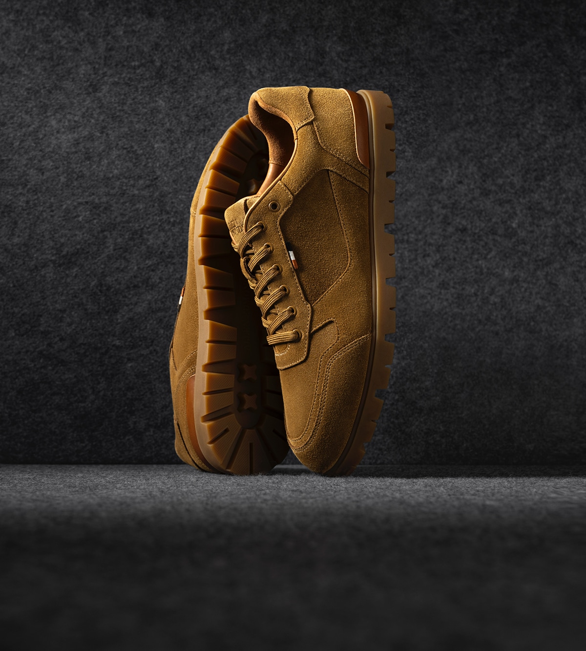 A pair of displayed men’s lace up sneakers in tan suede, displayed vertically.  