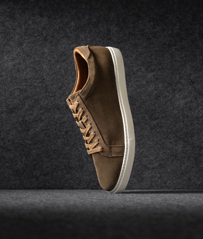 One single Allen Edmonds Courtside Lace Up Sneaker in brown corduroy, displayed vertically on its toe. 