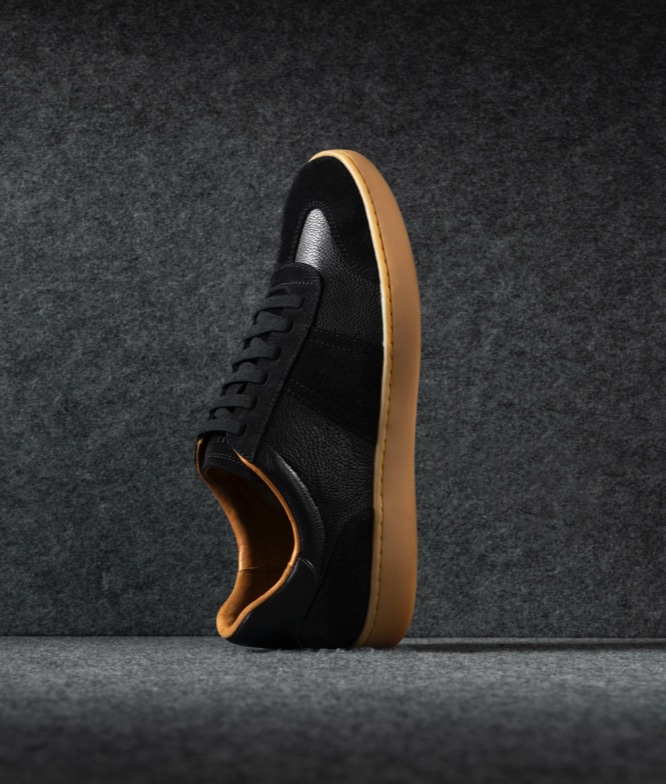 One single Allen Edmonds Ludlow Sneaker in black leather and suede positioned with the toe pointing upward. 
