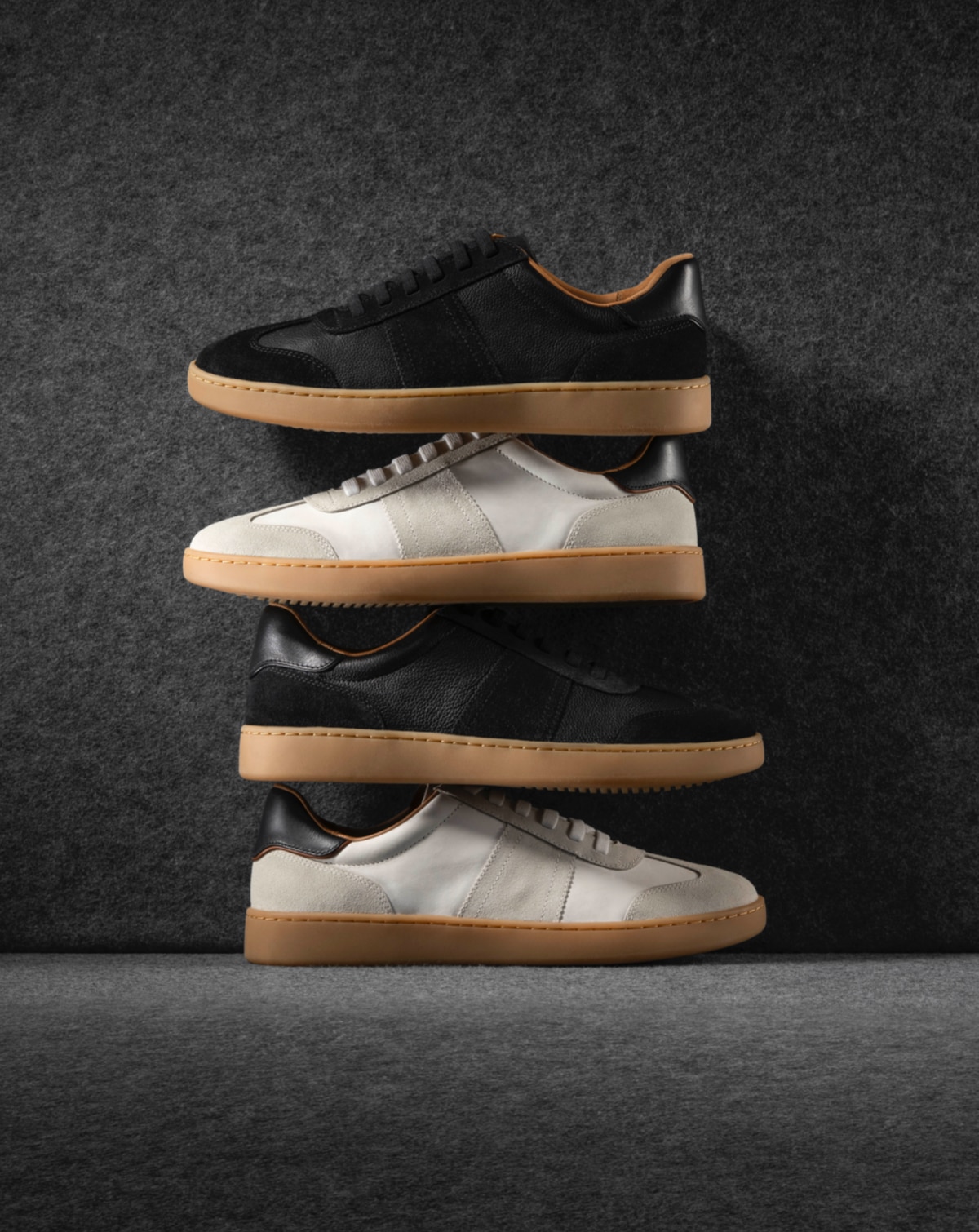 Two pairs of Allen Edmonds Ludlow Slip-On Sneakers, one black and one white, stacked on top of one another in an alternating pattern.  