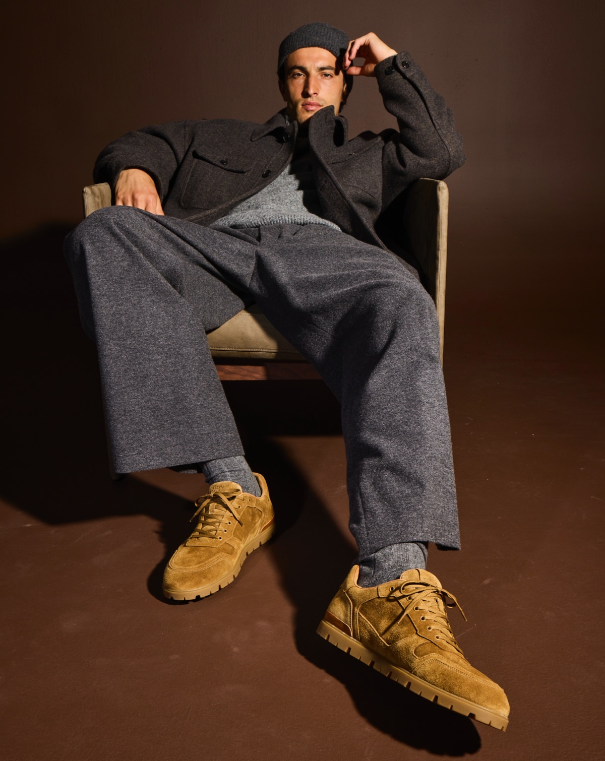 A male model sitting in a chair wearing the Allen Edmonds Vail Lug Sneaker in tan suede. 