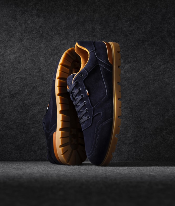 A pair of Allen Edmonds Vail Lug Sneakers in navy suede propped up vertically.