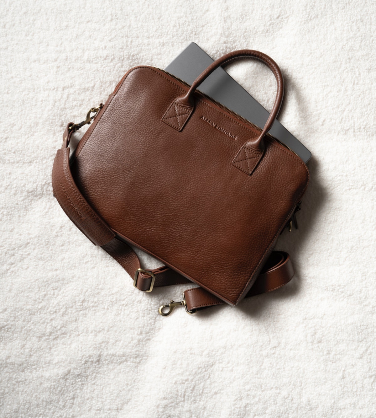 A men’s brown leather briefcase displayed at an angle with a laptop partially out of the bag.  
