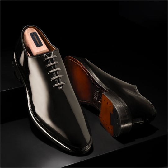 A pair of men’s black patent leather Oxford dress shoes with one laying on its side. 