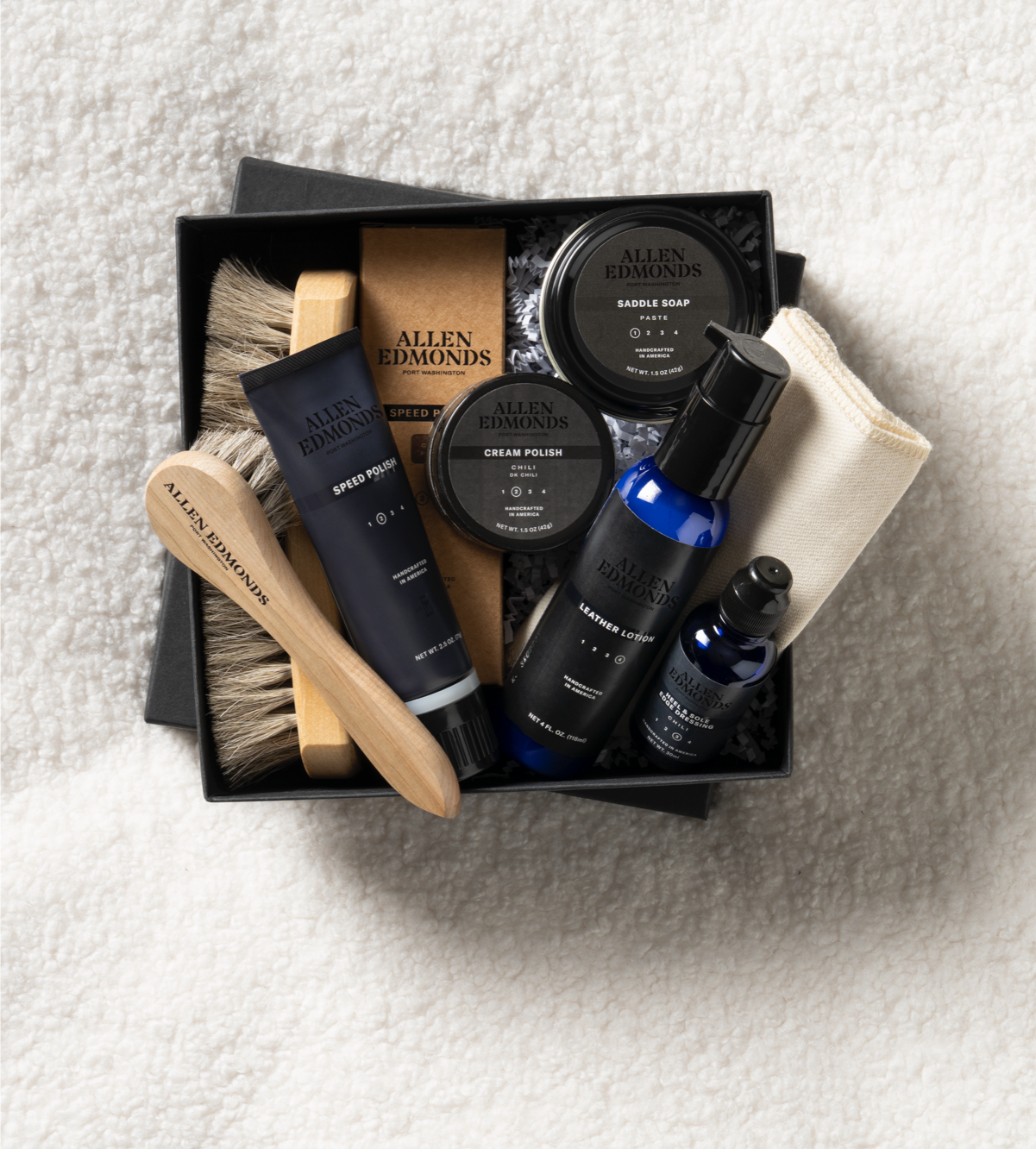A black box filled with various shoe care products, including shoe polish, a cleaning cloth, and a shoe brush.  