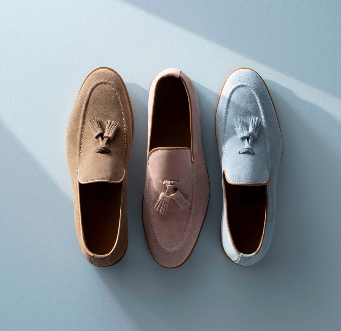 Allen Edmonds Randolph Tassel Loafers displayed in brown suede, pink suede, and sky blue suede against a light blue background