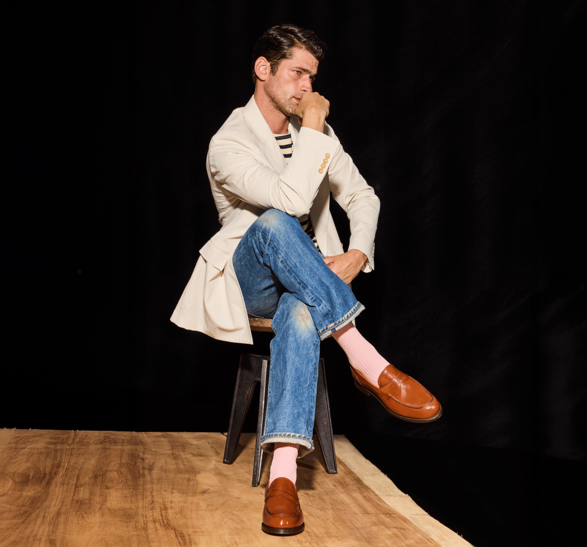 Tan leather Allen Edmonds penny loafers and pink socks worn by a man in a cream blazer and jeans sitting on a stool 