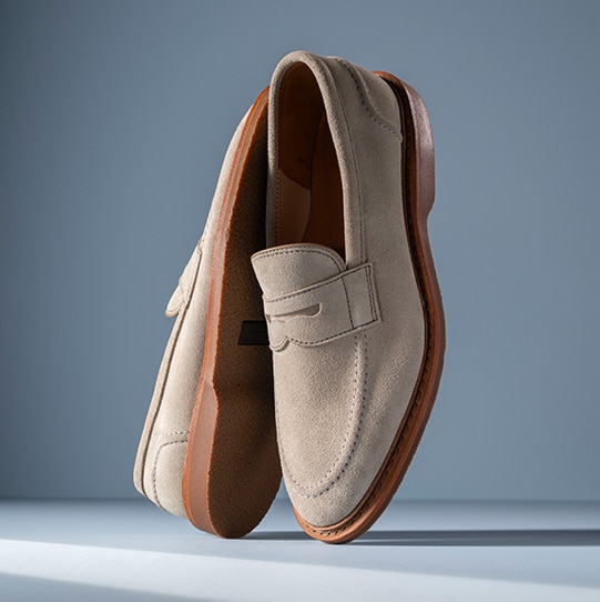 A pair of brown leather Chukka boots displayed vertically, showing the black dainite leather sole.